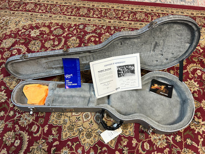Guitar case with accessories including a certificate of authenticity on a patterned rug.